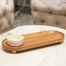 Load image into Gallery viewer, A long, oval wooden serving tray with small feet and a small white ceramic cup placed on one side.
