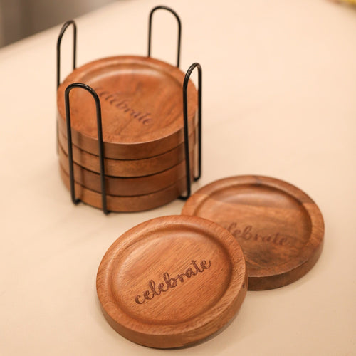 Set of wooden coasters with 'celebrate' engraving in a black holder on a light surface.