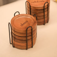 Load image into Gallery viewer, Set of wooden coasters with &#39;cheers&#39; engraving in a black holder on a light surface.
