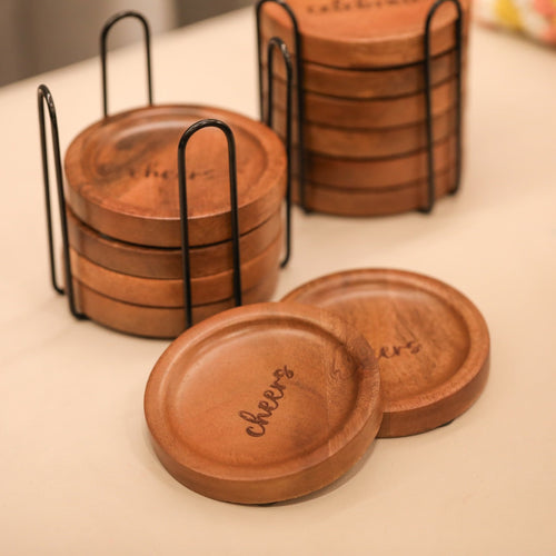 Set of wooden coasters with 'cheers' engraving in a black holder on a light surface.