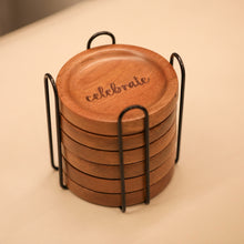 Load image into Gallery viewer, Set of wooden coasters with &#39;celebrate&#39; engraving in a black holder on a light surface.
